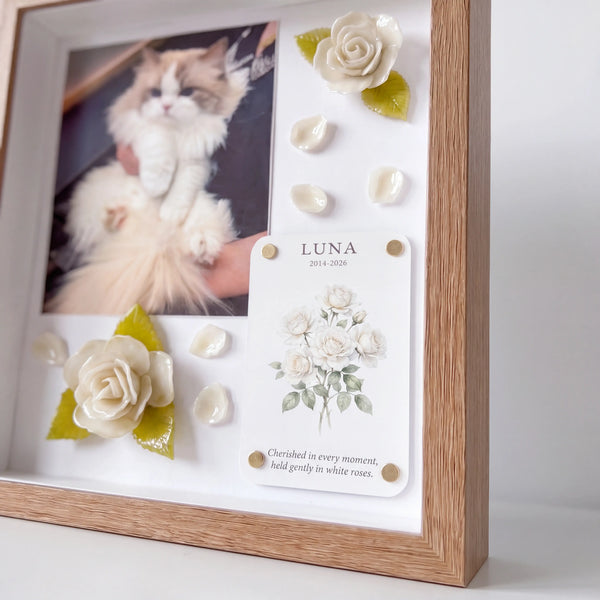 Angled view of a natural wood pet memorial shadow box with a cat photo and handmade white roses